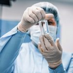 Profissional de saúde usando equipamento de proteção examina um frasco médico em um laboratório.
