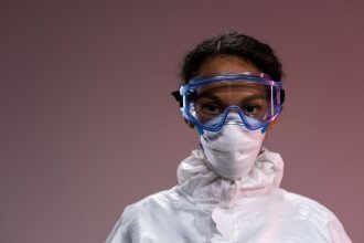 Profissional de saúde usando máscara, óculos de proteção e outros equipamentos de proteção individual.
