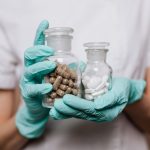 Profissional de saúde usando luvas segura frascos de vidro com cápsulas e comprimidos.