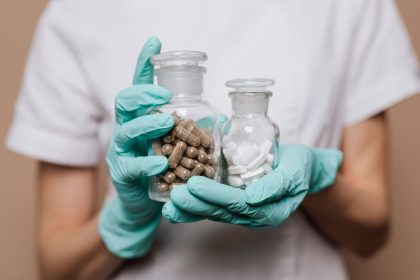 Profissional de saúde usando luvas segura frascos de vidro com cápsulas e comprimidos.