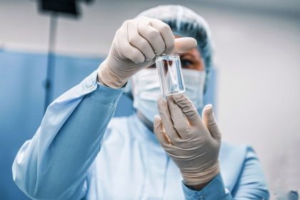 Profissional de saúde usando equipamento de proteção examina um frasco médico em um laboratório.