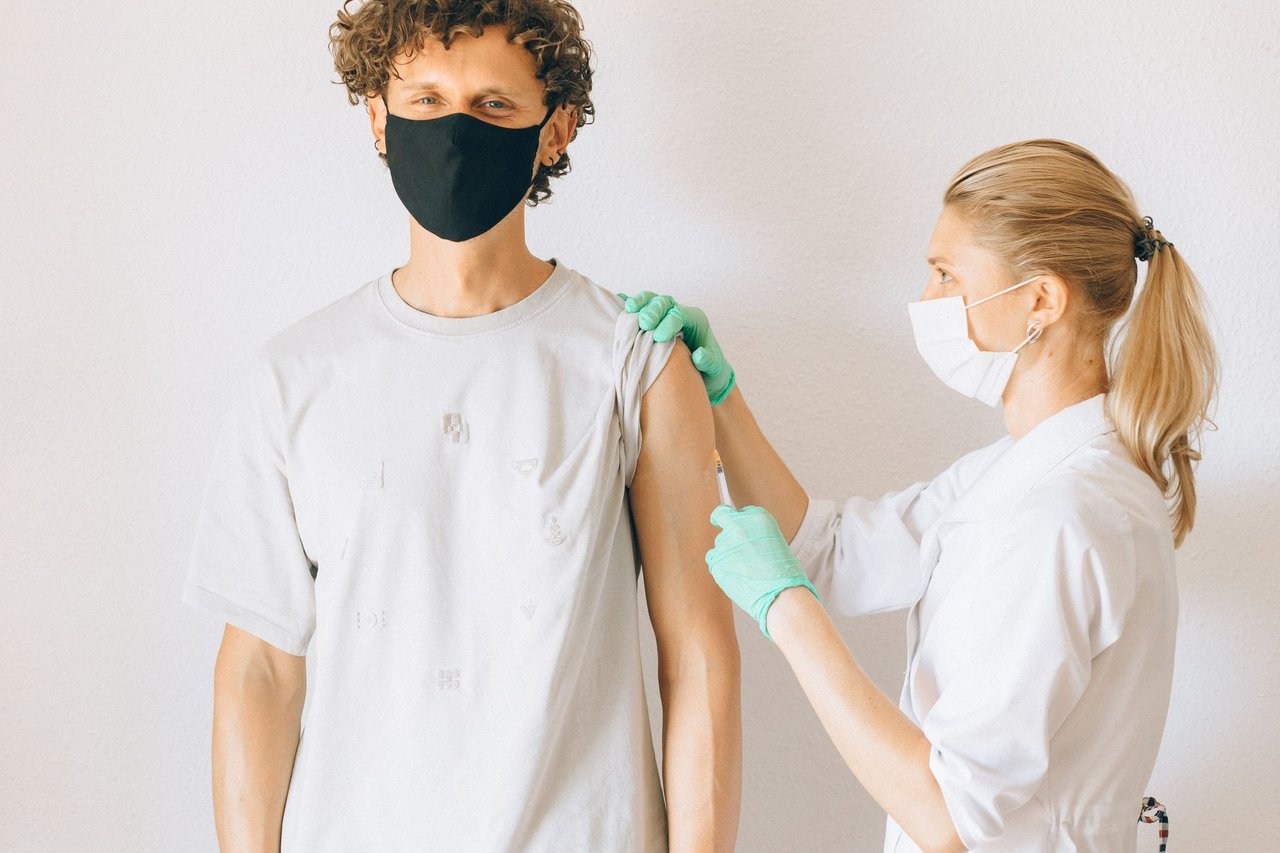 Profissional de saúde aplica uma vacina no braço de um homem mascarado em uma clínica.