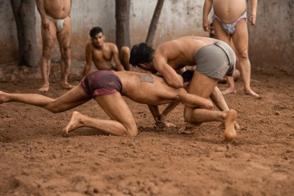 Dois homens participam de uma luta tradicional em uma arena de terra.