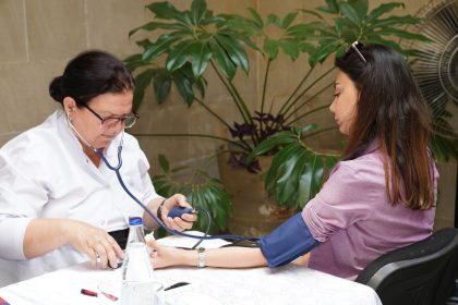 Profissional de saúde mede a pressão arterial de uma mulher em um ambiente externo.